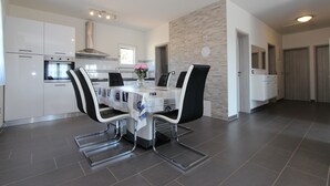 A modern kitchen with white cabinetry, a built-in oven, and a dining area with a table and chairs. - Apartment Mondelaco (Rovinj)