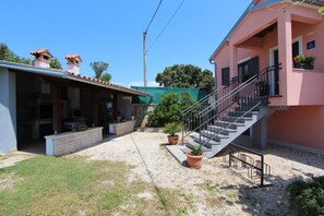 A residential building with a covered patio, a staircase, and potted plants.