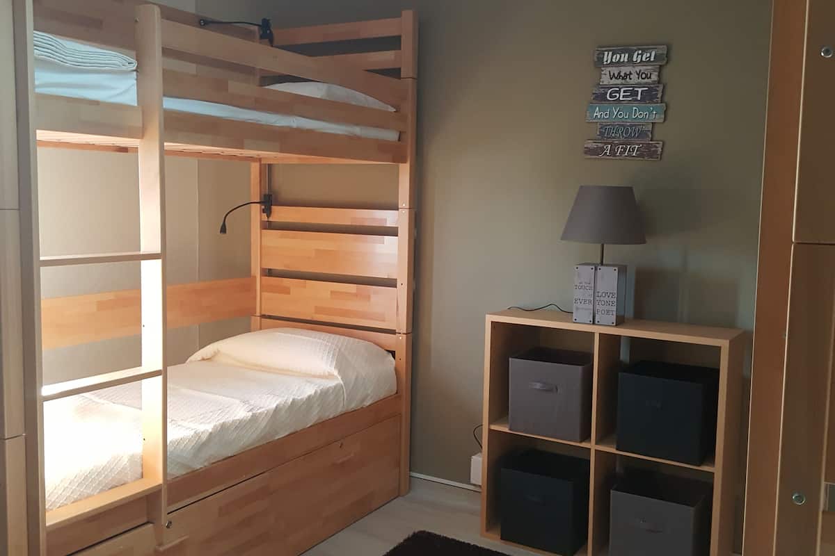 A bunk bed with a wooden frame, a bedside lamp, and storage boxes on a shelf.