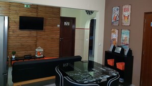 A reception area with a wooden wall, a flat-screen TV, a glass-top table, a bench, and a wall with posters advertising a beer bar. - Almancil Hostel (Loulé)