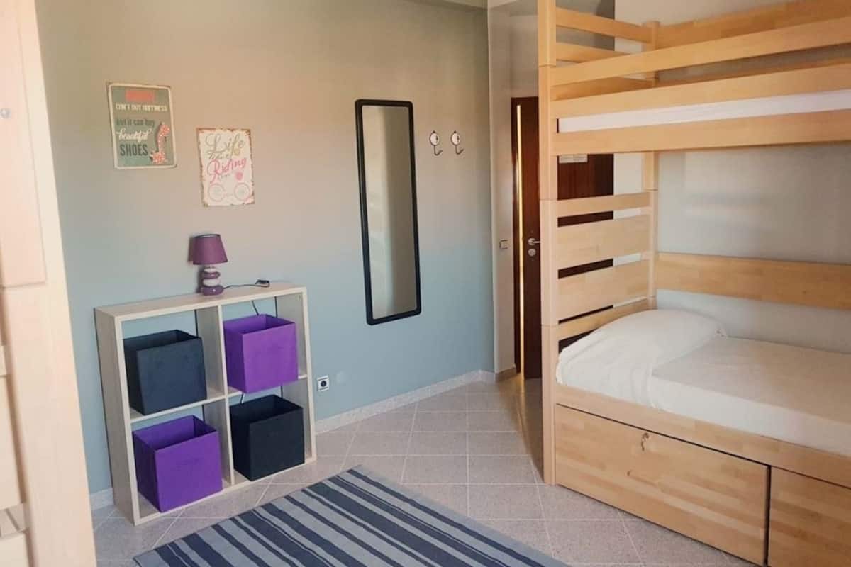 A room with a bunk bed, a small desk with a lamp, and storage boxes.