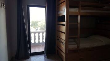 Ein Zimmer mit einem Holzstockbett, einer Schiebetür zu einem Balkon und einem kleinen Tisch.