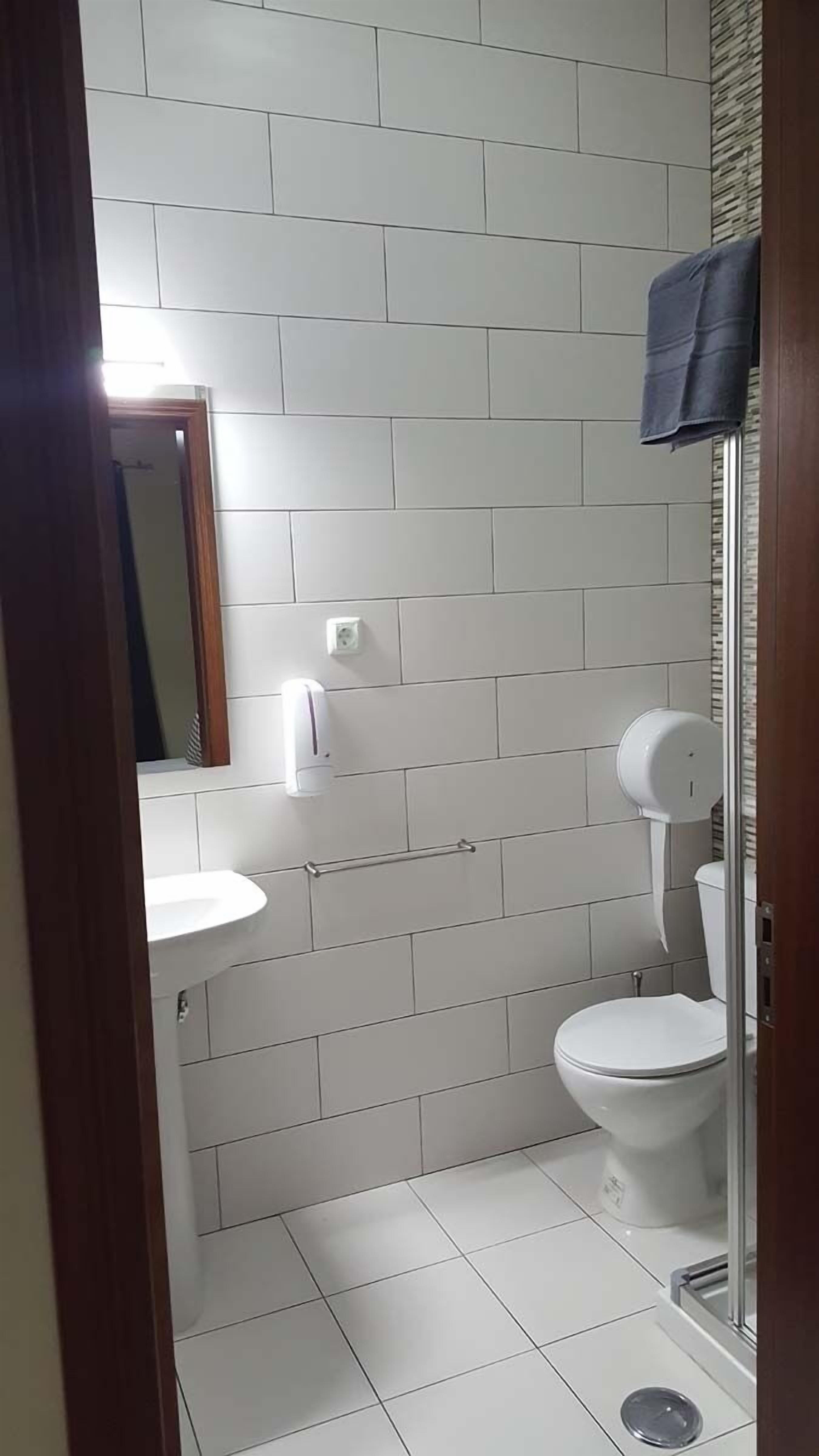 Ein kleines, modernes Badezimmer mit weißen Fliesen, einem weißen Waschbecken, einer Toilette und einer Duschkabine.
