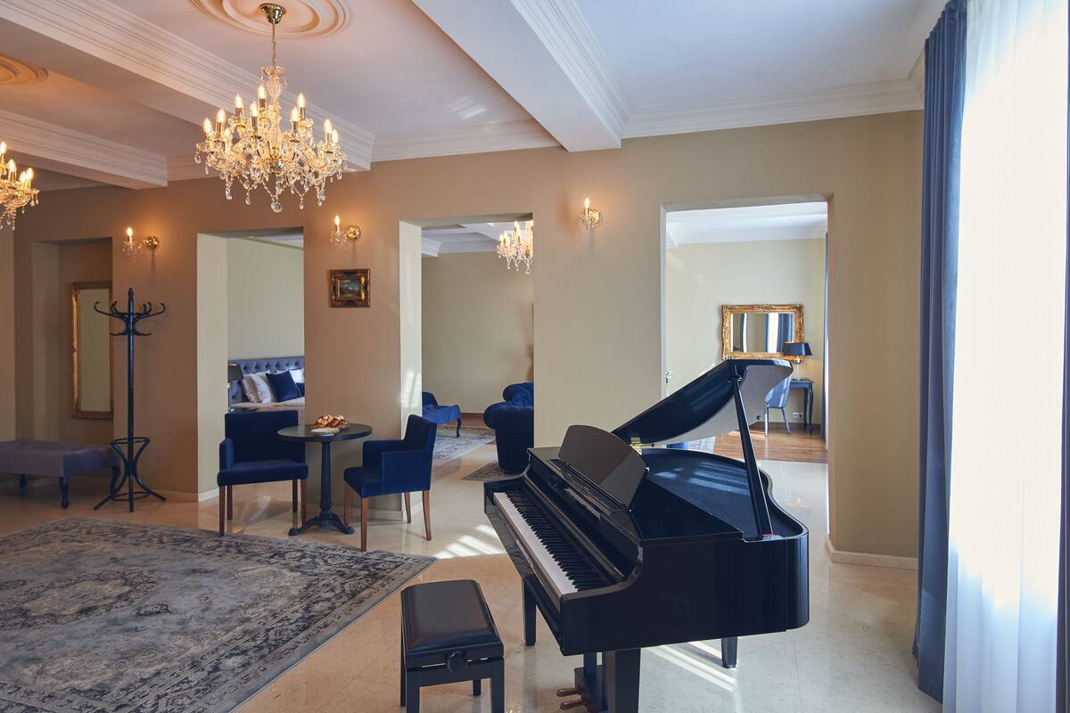 A grand piano in a spacious living room with a chandelier, blue sofas, and a large rug.