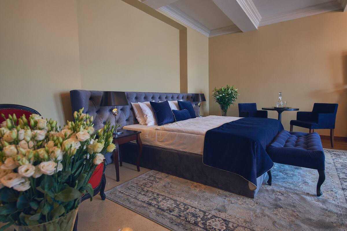 A bedroom with a large bed, bedside tables, a small table with chairs, and a vase of flowers.