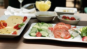 A table set with various dishes including sliced tomatoes, cucumbers, and a bowl of salad, with a glass of drink and a pineapple on the table. - Hotel Bogoria (Kraków)