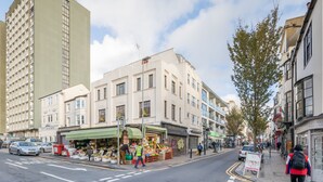 Une vue de rue avec une rangée de boutiques, dont un étal de fruits et une pharmacie.