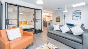 Un salon moderne avec un canapé, un fauteuil et un lit à l’arrière-plan.
