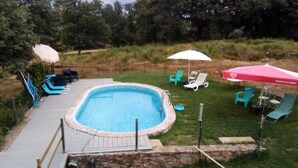 Une piscine rectangulaire bordée de pierres, entourée d’une pelouse et d’un muret en pierre. On y trouve deux parasols et plusieurs chaises longues.
