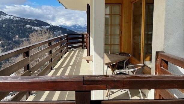 A balcony with a wooden railing, a table, and chairs, overlooking a mountainous landscape. - Bright and warm apartment for up to 4 people, on the ground floor of a chalet with two apartments. I (St-Luc)