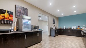 Une cuisine moderne avec des meubles de couleur sombre, un distributeur de jus de fruits, un four à micro-ondes et une machine à café.