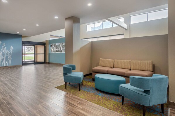 A spacious lobby with a wooden floor, a blue armchair, a brown sofa, and a colorful rug. - Sleep Inn & Suites Bricktown - near Medical Center (Oklahoma City)