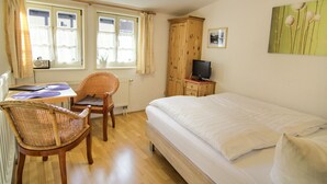 A bedroom with a bed, a chair, a table, a television, and a wardrobe. - Coach house - Small house on two levels (Quedlinburg)