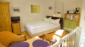 A bedroom with a bed, a television on a wooden cabinet, a wicker chair, a dining table, and a coffee machine on a shelf. - Coach house - Small house on two levels (Quedlinburg)