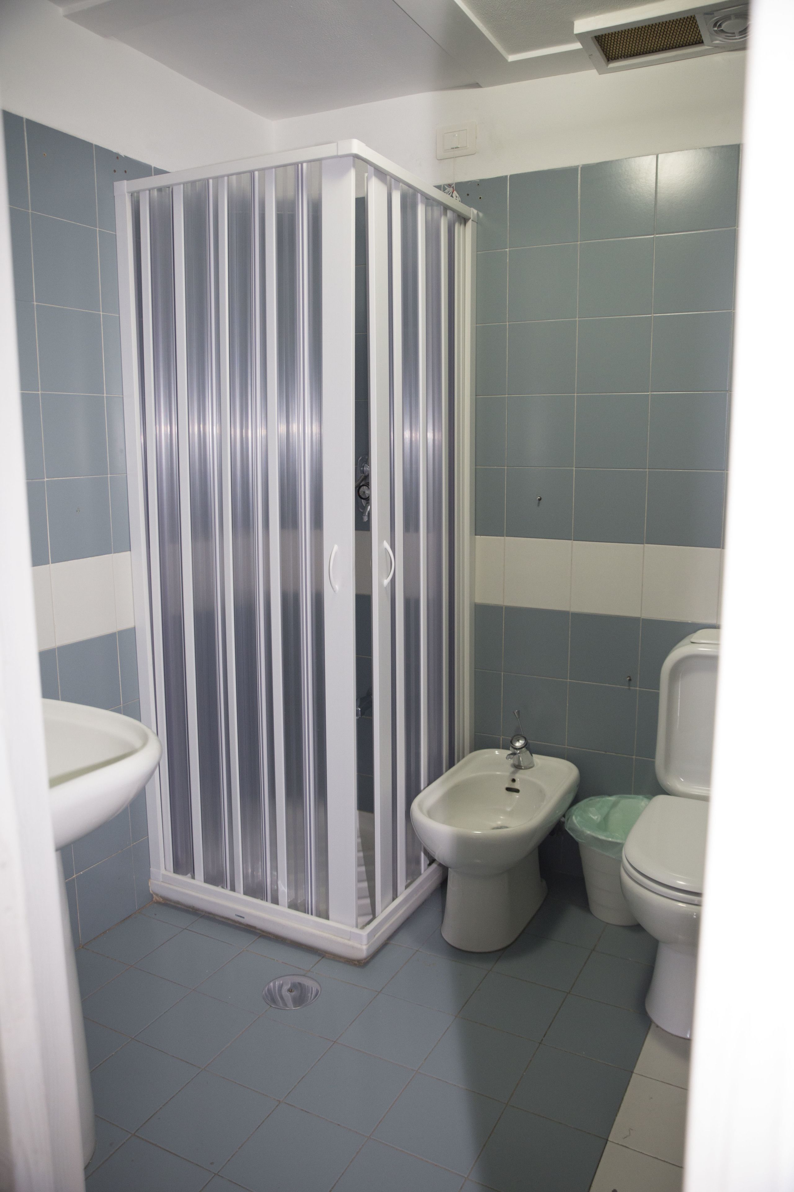 A bathroom with a shower enclosure, bidet, toilet, and sink.