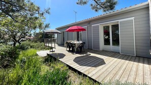 A wooden deck with a table and chairs, a red umbrella, and a sliding glass door. - Family Home Near Marais Girard Beach, Quiet Cul-de-Sac, 9 Sleeps, 2 Terraces, WiFi (Bretignolles-sur-Mer)