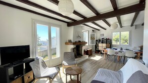 A spacious living room with a television, seating, a fireplace, and a dining area with a view. - Family Home Near Marais Girard Beach, Quiet Cul-de-Sac, 9 Sleeps, 2 Terraces, WiFi (Bretignolles-sur-Mer)