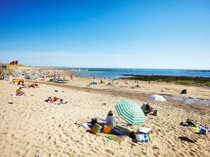 A sandy beach with people sunbathing and swimming, umbrellas, and beach chairs.