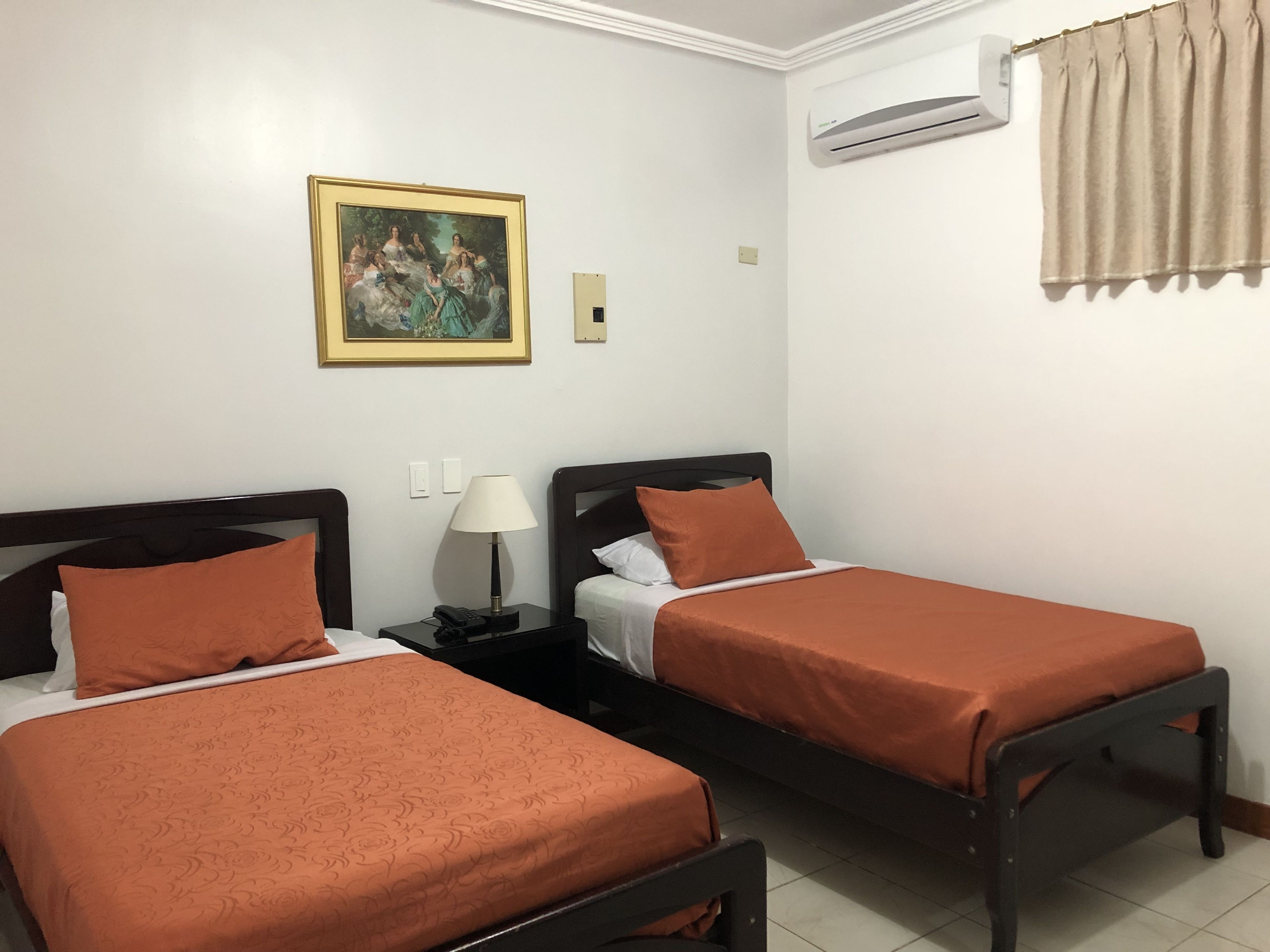 Una habitación con dos camas individuales, una mesita de noche con lámpara, aire acondicionado y un cuadro en la pared.