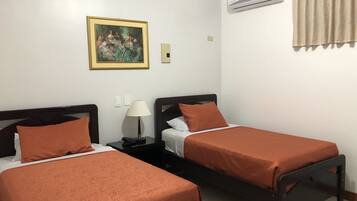 Una habitación con dos camas individuales, una mesita de noche con lámpara, aire acondicionado y un cuadro en la pared.