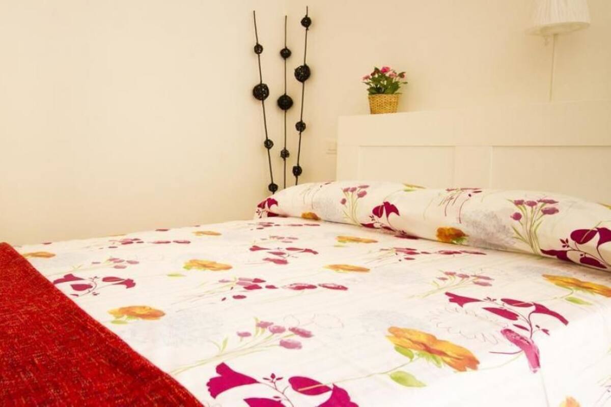 A bed with a floral bedspread, a red throw blanket, and a wall-mounted decoration.