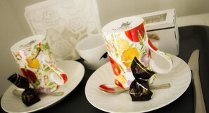 Two floral-patterned cups on saucers, a spoon, and a small chocolate bar on a table. - Agriturismo La Casa nel Cielo (San Paolo di Jesi)