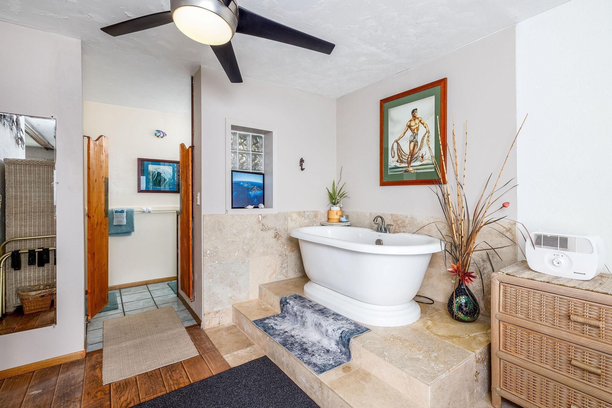 A bathroom with a freestanding bathtub, a ceiling fan, and a framed picture on the wall.