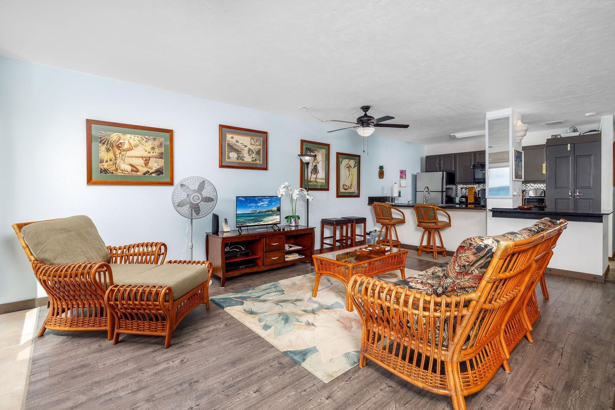 A living room with wicker furniture, a ceiling fan, and framed artwork on the walls.