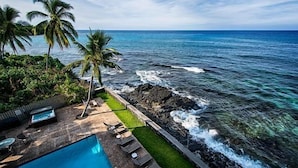 A poolside area with lounge chairs, a hot tub, and a view of the ocean.