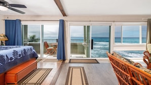A room with a bed, a balcony with a view of the ocean, and a chair.