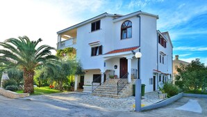 A two-story building with a balcony, a staircase leading to the entrance, and a garden with palm trees. - Ina Apartments (Zadar)