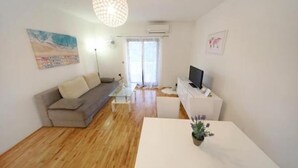 A modern living room with a sofa, a coffee table, and a TV. There is a painting on the wall and a window with curtains. - Ina Apartments (Zadar)