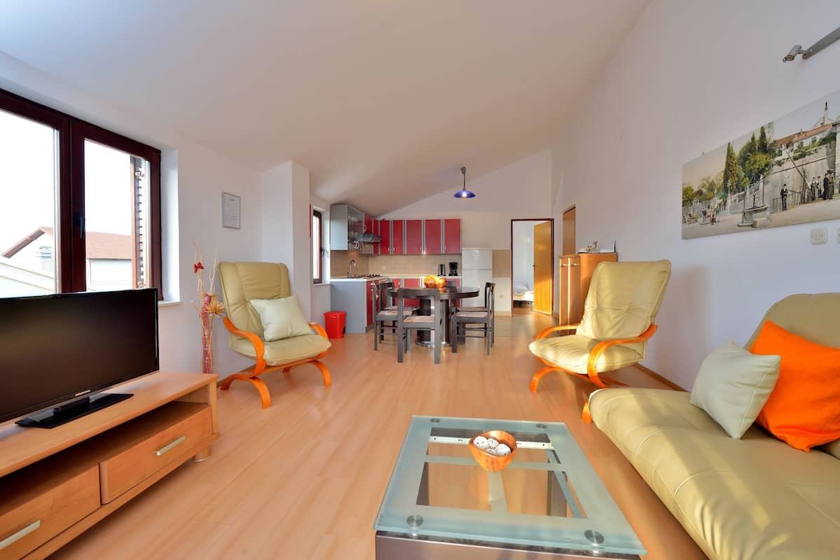 A modern living room with a TV, sofa, and coffee table. A dining area with chairs and a table is visible in the background.