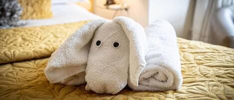 Une serviette blanche, soigneusement pliée et ornée d’un motif représentant un lapin, est posée sur un lit recouvert d’une couette jaune matelassée.