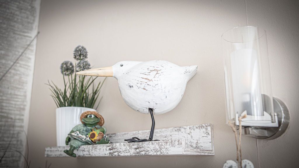 A bird-shaped sculpture on a shelf, a potted plant, and a wall-mounted light fixture.