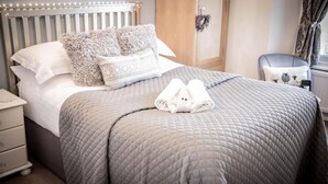 A neatly made bed with a grey quilt, two fluffy pillows, and a pair of folded towels on the bed. - Hillsdale in Ambleside (Ambleside)
