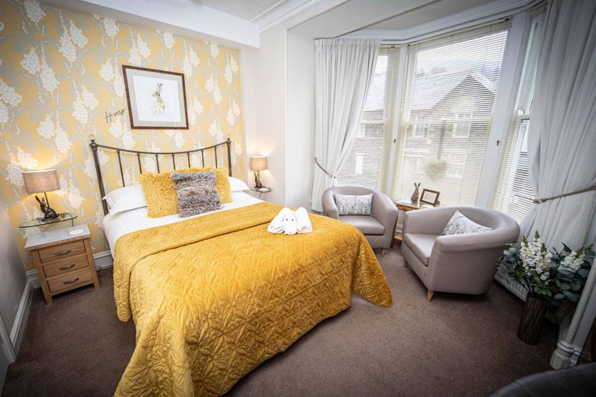 A hotel room with a bed, two bedside tables, a chair, and a window with curtains.