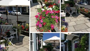 A courtyard with outdoor seating, a variety of flowers, and a white umbrella. - Hillsdale in Ambleside (Ambleside)