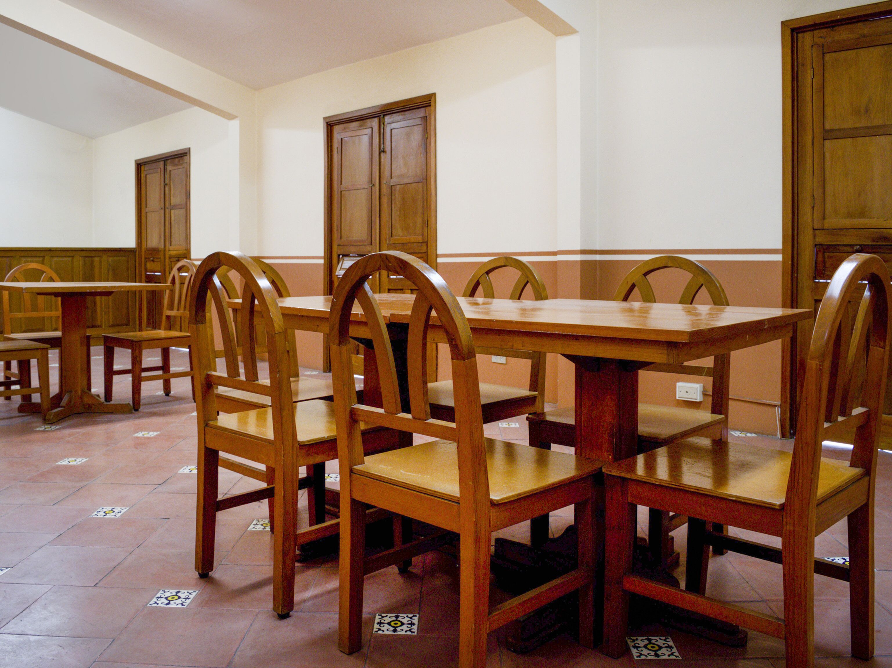A dining area with wooden tables and chairs, tiled flooring, and wooden doors.