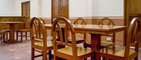 A dining area with wooden tables and chairs, tiled flooring, and wooden doors.
