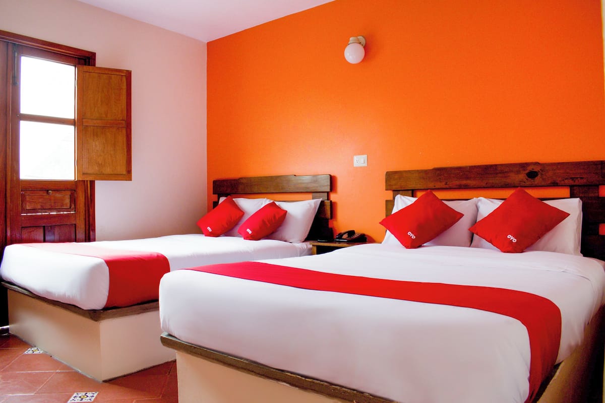 Two beds with red and white bedding, a wooden headboard, and a window with a wooden frame.