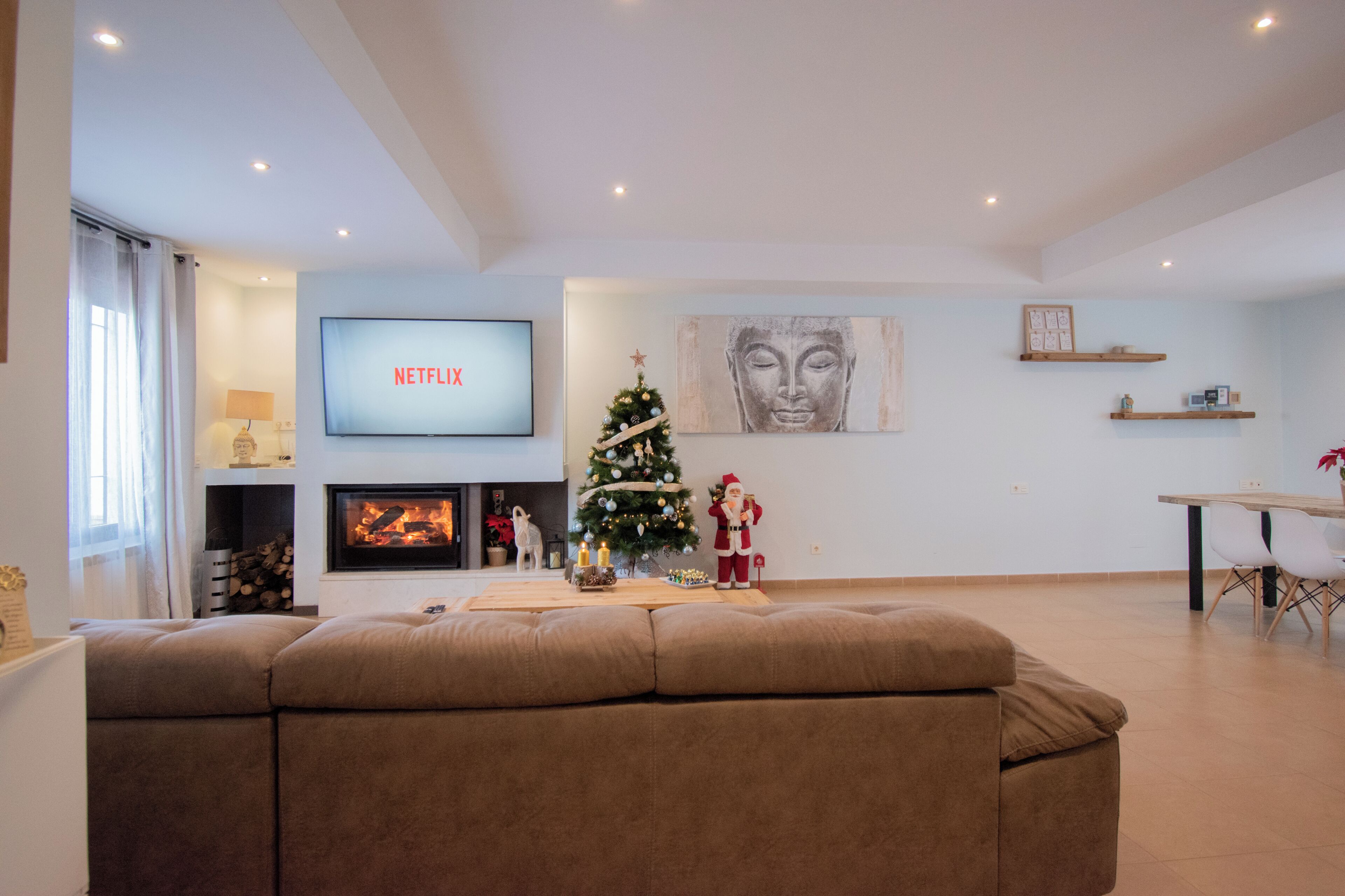 A living room with a fireplace, a Christmas tree, a sofa, a TV, and a Buddha painting.