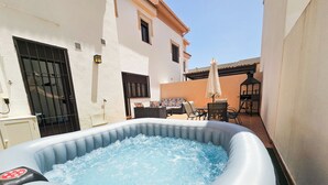 Un jacuzzi gonflable installé dans une cour, avec un bâtiment blanc, un portail noir et du mobilier d’extérieur.