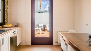 Une cuisine moderne avec des armoires blanches, un plan de travail en bois et une vue sur un espace de détente extérieur, accessible par une porte vitrée.