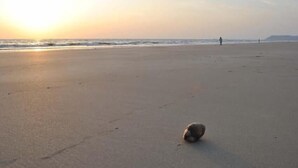 Une plage avec un seul ballon sur le sable et une personne au loin.