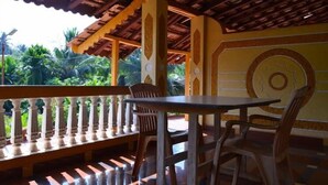 Un espace extérieur aménagé avec une zone de repos couverte, comprenant une table et des chaises en bois, une rambarde décorative et une vue sur une végétation luxuriante.