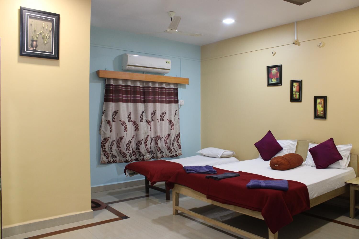 Una habitación de hotel con cama, ventana con cortinas, equipo de aire acondicionado y una pequeña estantería.