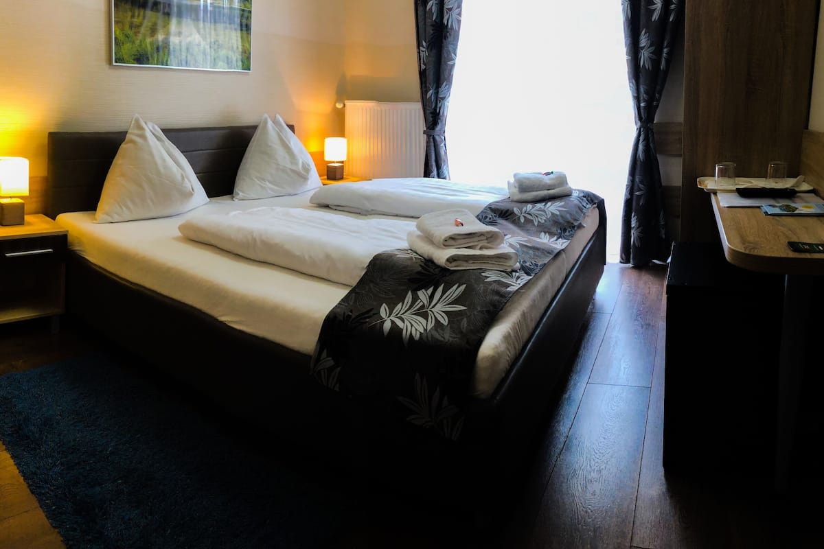 Una habitación de hotel con cama, lámparas de noche, un escritorio y una ventana con cortinas.