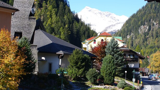 A mountain town with buildings, a road, and a snow-capped mountain in the background. - Hotel Mallnitz Appartements (Mallnitz)