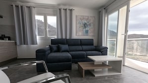 Un soggiorno moderno con un divano blu scuro, un tavolino bianco e vista su un paesaggio montuoso attraverso ampie finestre.